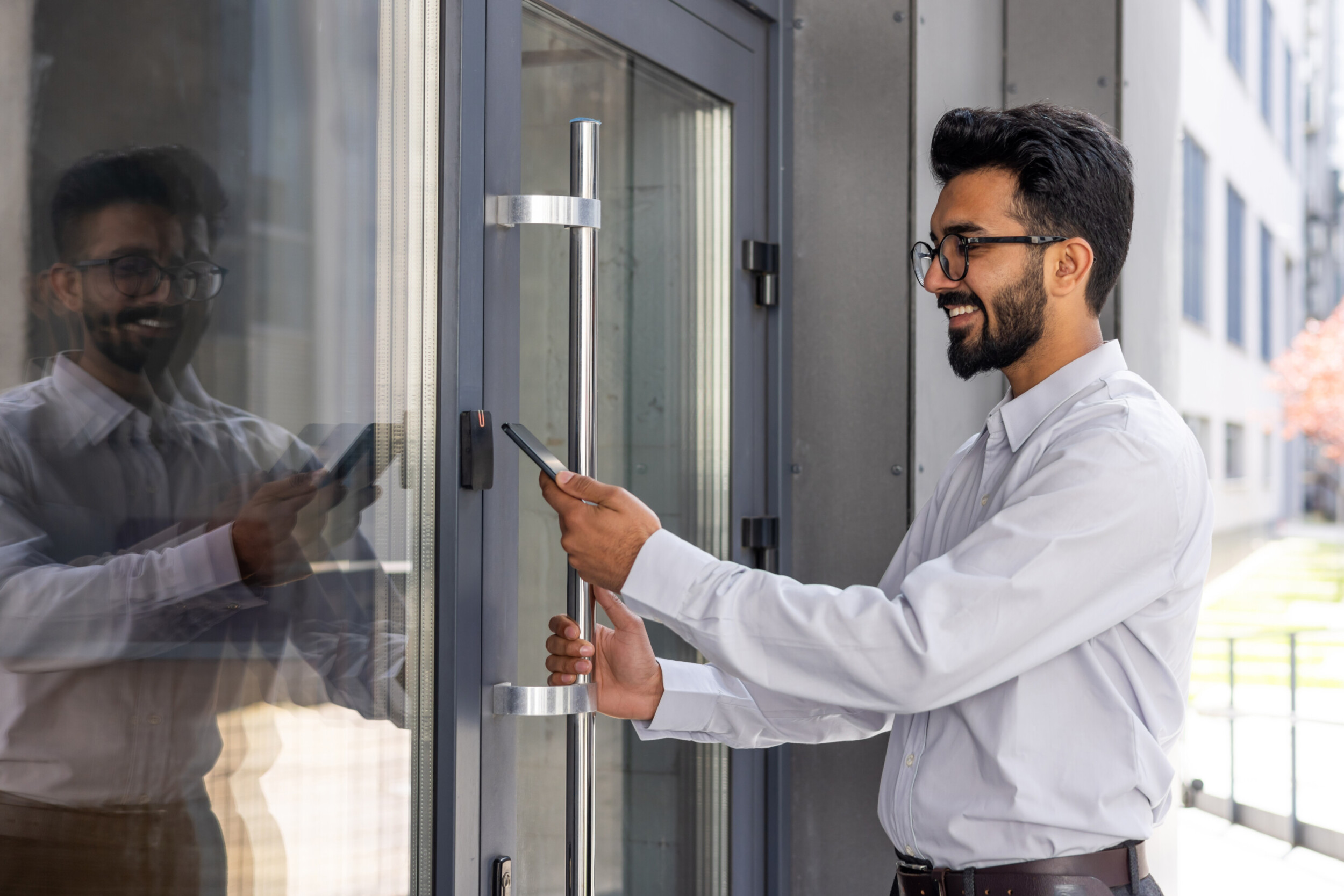 Young businessman using phone to open office door of building, man happy using wireless access, businessman going to work happy smiling