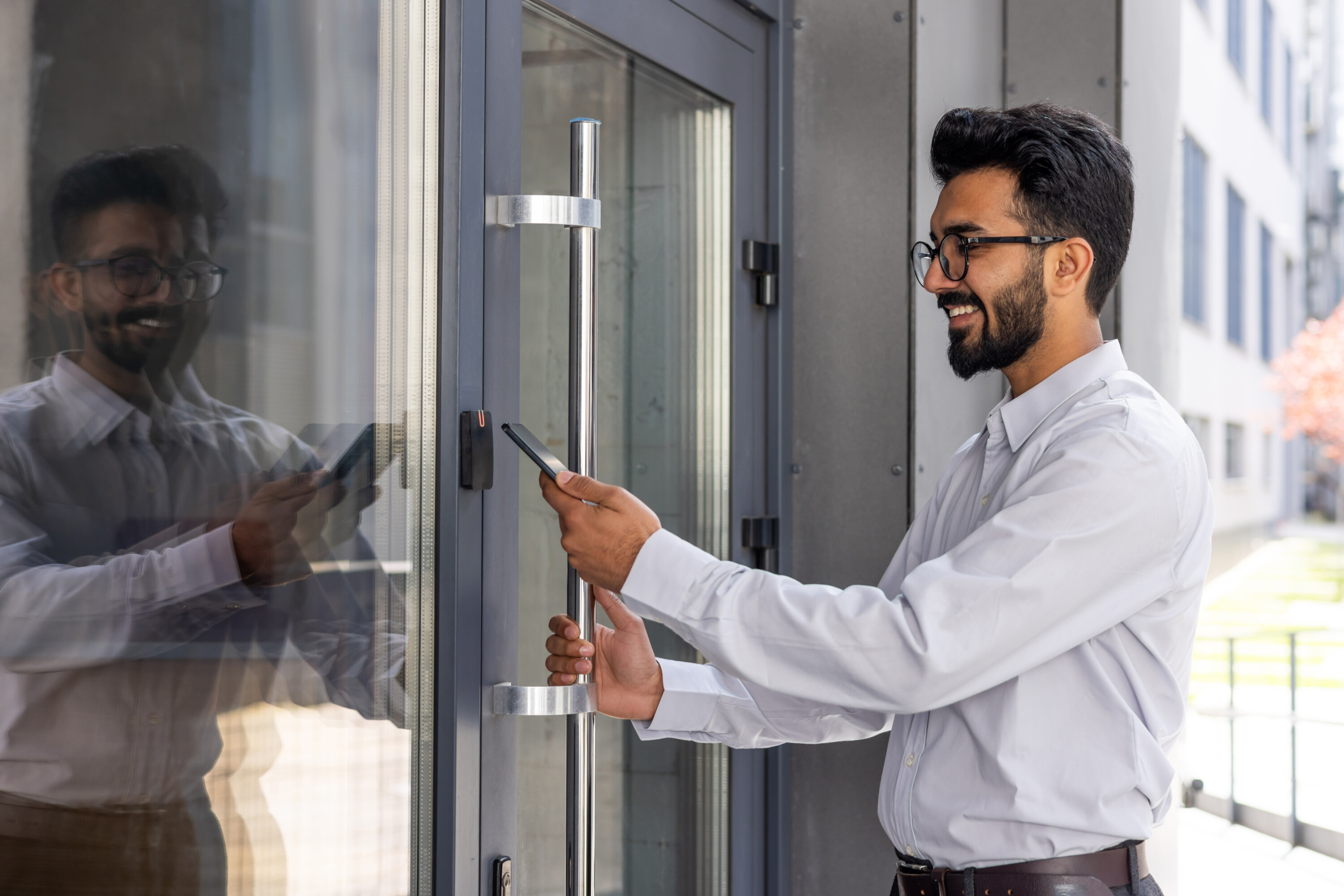 Young businessman using phone to open office door of building, man happy using wireless access, businessman going to work happy smiling