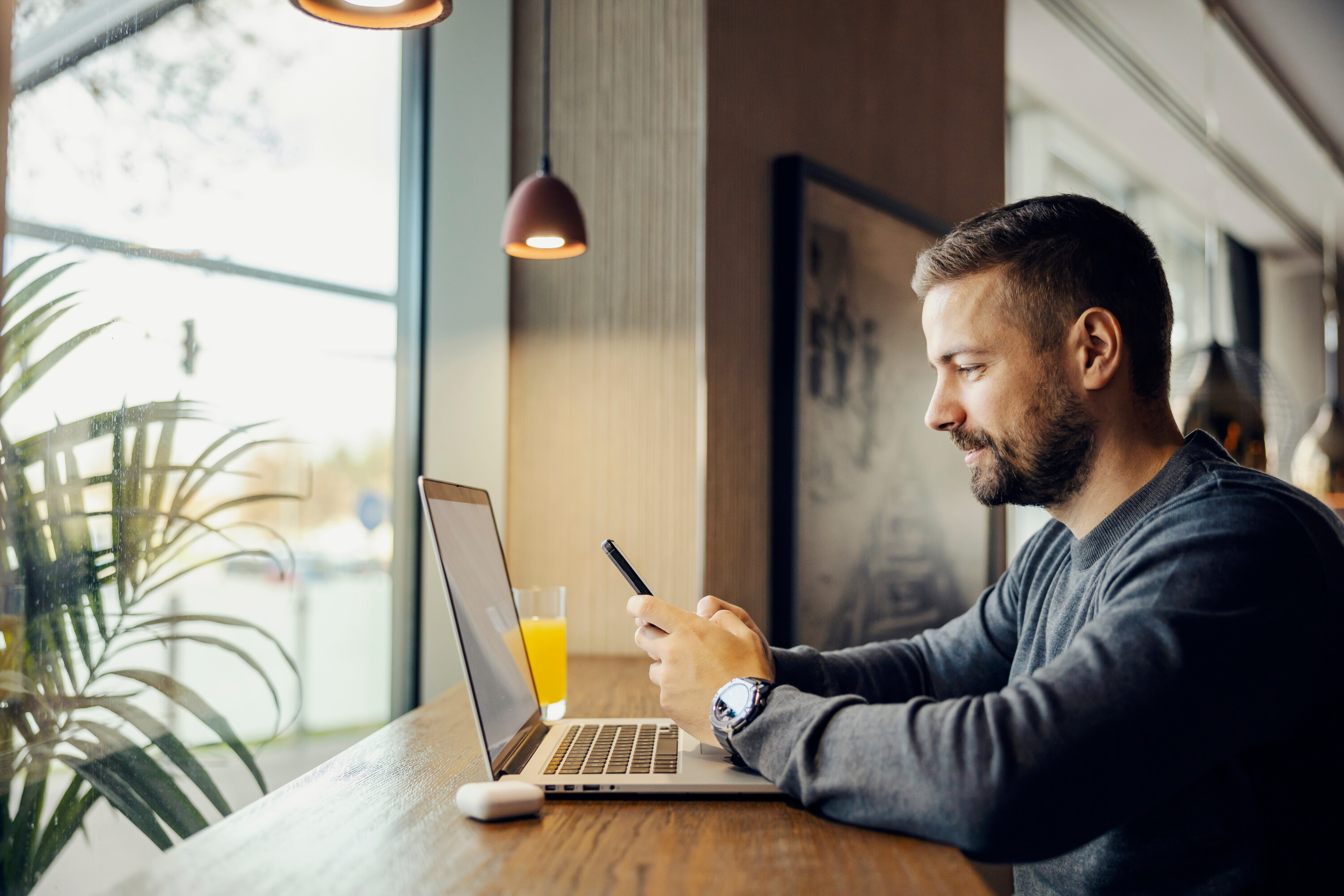 A busy digital marketer is sitting in coffee shop and working on social media by using phone and laptop.