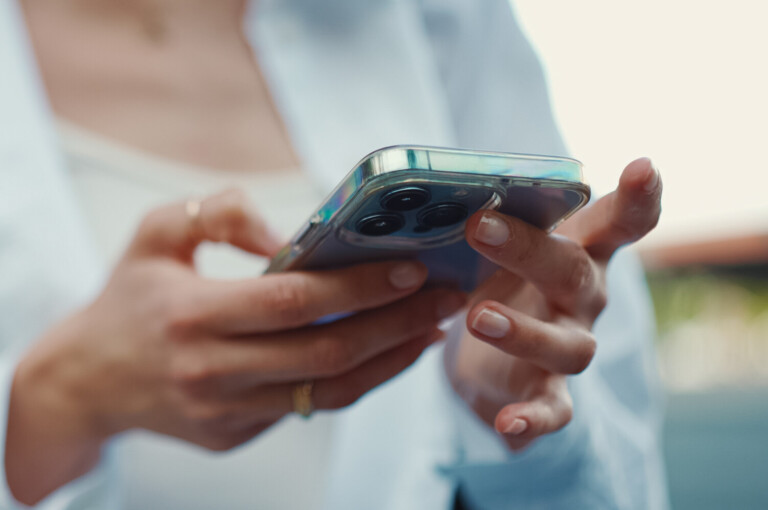 Closeup of young woman holds smartphone in her hands and scrolls through the news feed. Close-up of girl hand uses mobile phone outdoors